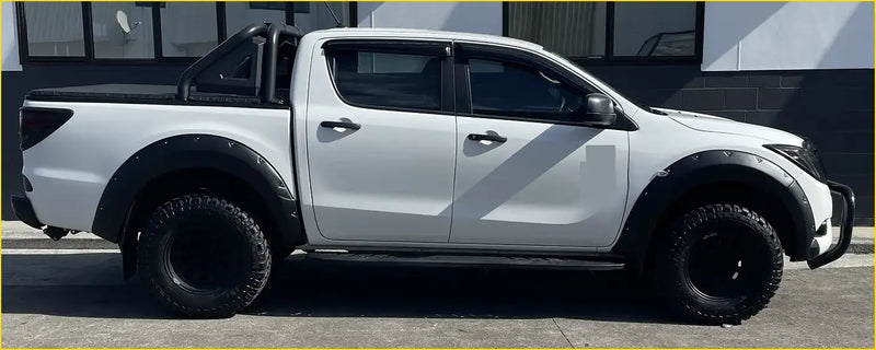 White mazda bt-50 pickup with black bolt flares rugged off-road tires and a roll bar for tough terrain use