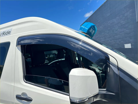 A bright blue dome-shaped taxi sign mounted on the roof of a white van with toyota hiace door visors weather shields