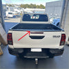 Back view of white toyota hilux with durable textured black tailgate cover featuring black handle and red taillights