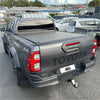 Dark gray metallic toyota hilux revo with electric roller shutter tonneau cover over truck bed from back side view