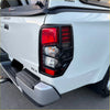 Black plastic taillight cover with red and clear lens sections shown from the back on a white mitsubishi triton 2019-2023 pickup truck