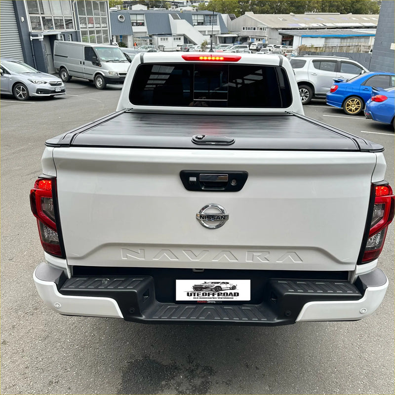 White nissan navara pickup truck with black manual roller shutter tonneau cover shown from the back side