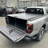 Black roll-up manual roller shutter tonneau cover on the back of silver volkswagen amarok 2023+ pickup truck
