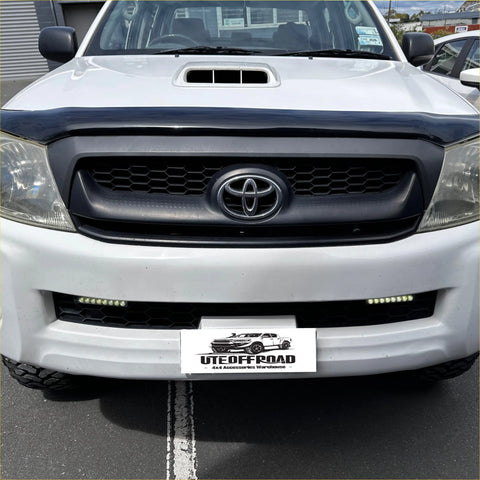 White toyota hilux pickup truck with black front grille and chrome emblem featuring monsoon and bonnet guard