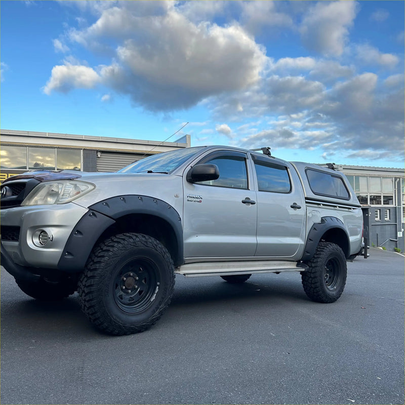 Silver toyota hilux pickup with matte black monster flare bolt style fender flares and rugged off-road tires