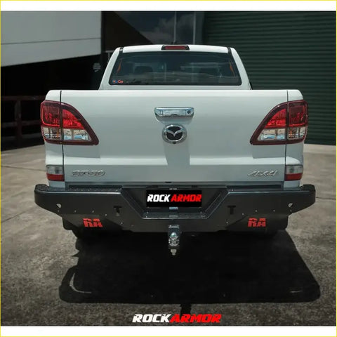 Rear view of black steel rockarmor elite rear step bumper with red accents and towbar on white mazda bt50 4wd ute