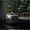 White toyota land cruiser 4wd with rockarmor gt hoop steel bullbar and offroad tires parked under leafy trees