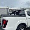 Black soft tonneau cover with integrated roll-up design and perforated metal railings on white nissan navara d40 pickup back side