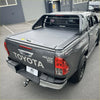 Gray toyota hilux sr5 limited with ruggedized manual roller shutter black tonneau cover shown from back side