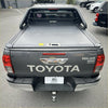 Back view of dark gray toyota hilux srs limited with a ruggedized manual black roller shutter tonneau cover