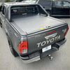 Dark gray toyota hilux pickup with black manual roller shutter tonneau cover and chrome accents shown from the back side