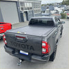 Dark gray toyota hilux pickup truck back with ruggedized manual roller shutter tonneau cover over the bed
