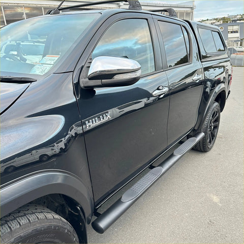 Black toyota hilux pickup with chrome mirrors and black stainless steel 4 inch oval tube running boards visible from side