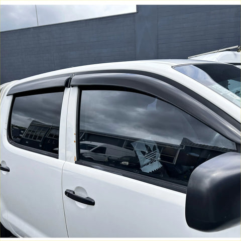 Black plastic window visors installed on a white toyota hilux vigo for weather protection and style