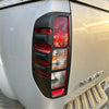 Black plastic tailgate protector with vertical slats around red clear taillight on silver nissan navara d40 pickup
