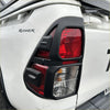 Black plastic taillight cover with red and clear lenses mounted on white toyota hilux 2015-2020 sr sr5 sr5 cruiser