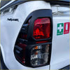 Black plastic taillight cover with red lens and clear reflector on the back of a white mitsubishi triton frerunner pickup truck