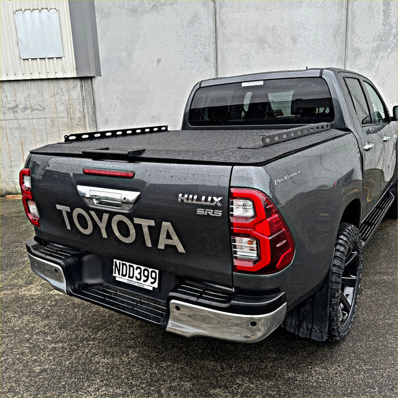 Dark gray toyota hilux sr5 double cab with black tomahawk aluminium hardlid and off-road tires shown from the back side